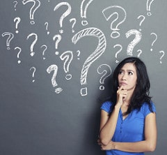 Question Marks on Black board with Woman looking Confused