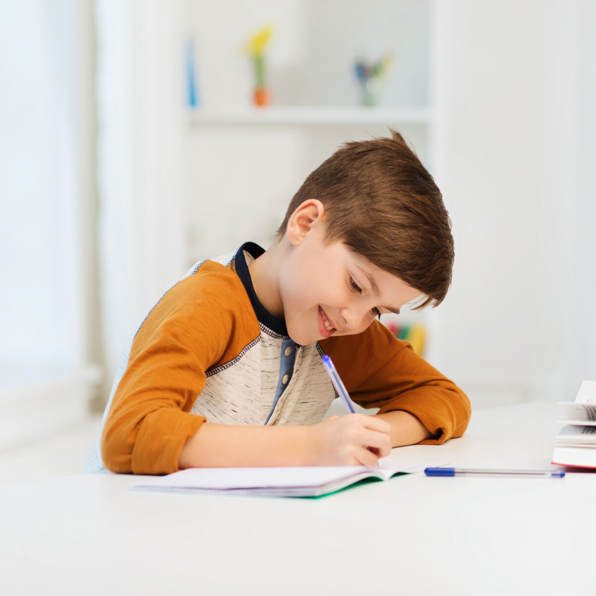 smiling student boy writing to notebook at home